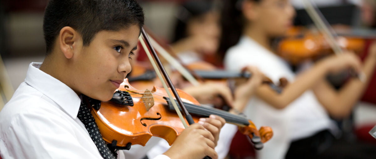 Young violinists play in open concert with the orchestra. Focus on foreground.